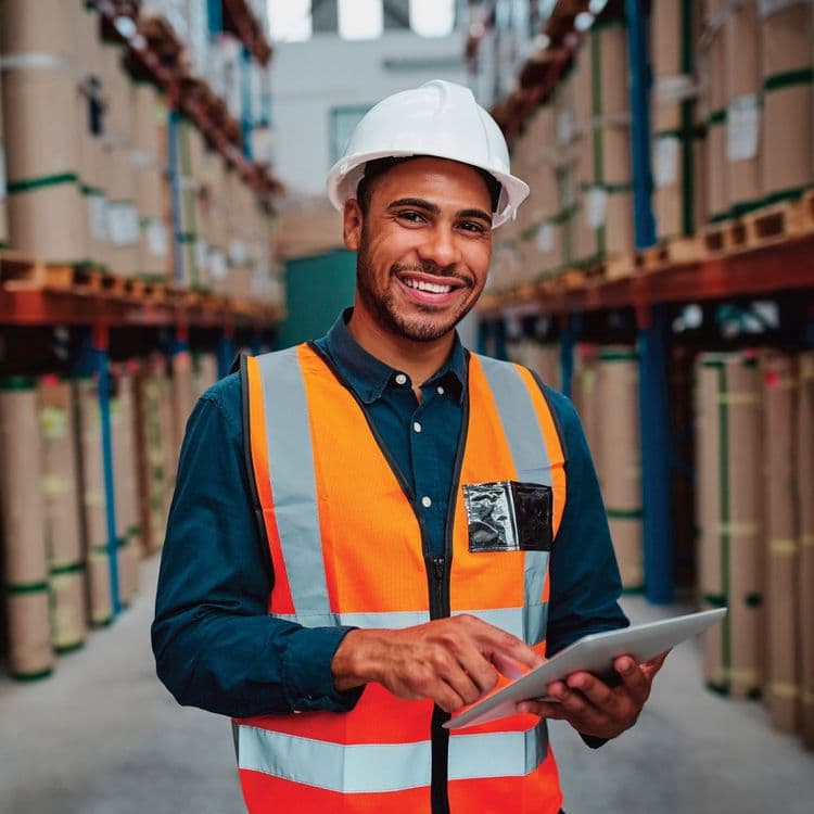 A man wearing a hard hat and construction vest smiling while tapping on a tablet.