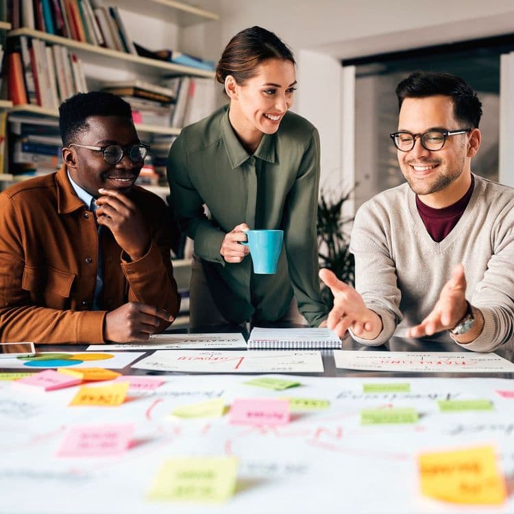 Two men and a woman with a coffee mug working together on a project.